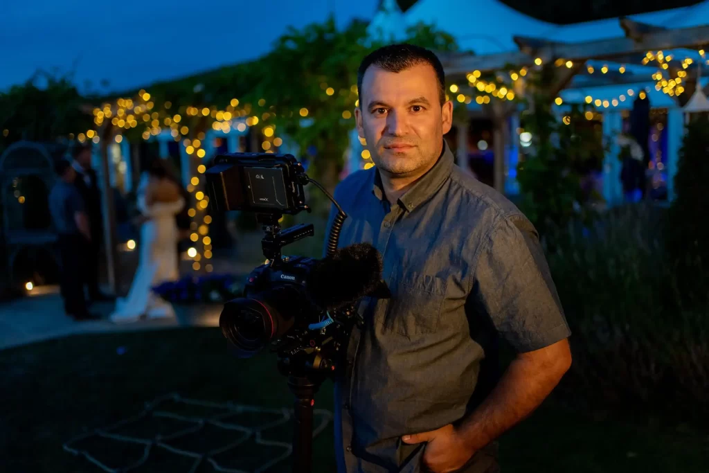 VasPhotography holding camera on a monopod  looking at the lens . evening scene with festoon lights in the background