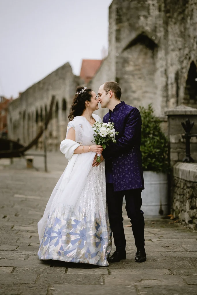 A newly married bride and groom holding hands, smiling, and posing for portraits outdoors against scenic stone walls and garden pathways, captured beautifully by VasPhotography specializing in small wedding photography in Southampton