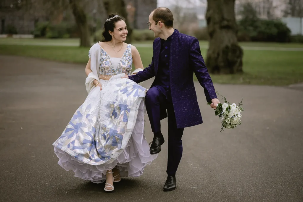A newly married bride and groom holding hands, smiling, and posing for portraits outdoors against scenic stone walls and garden pathways, captured beautifully by VasPhotography specializing in small wedding photography in Southampton