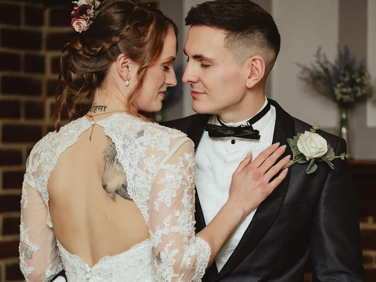 Candid wedding photographer capturing intimate bride and groom portrait with lace back dress and black tuxedo indoors.