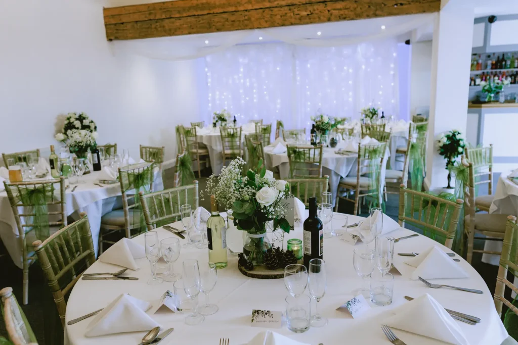 Wedding reception room dressed with green organza sashes and rose centrepieces at The Angel Hotel, Alton